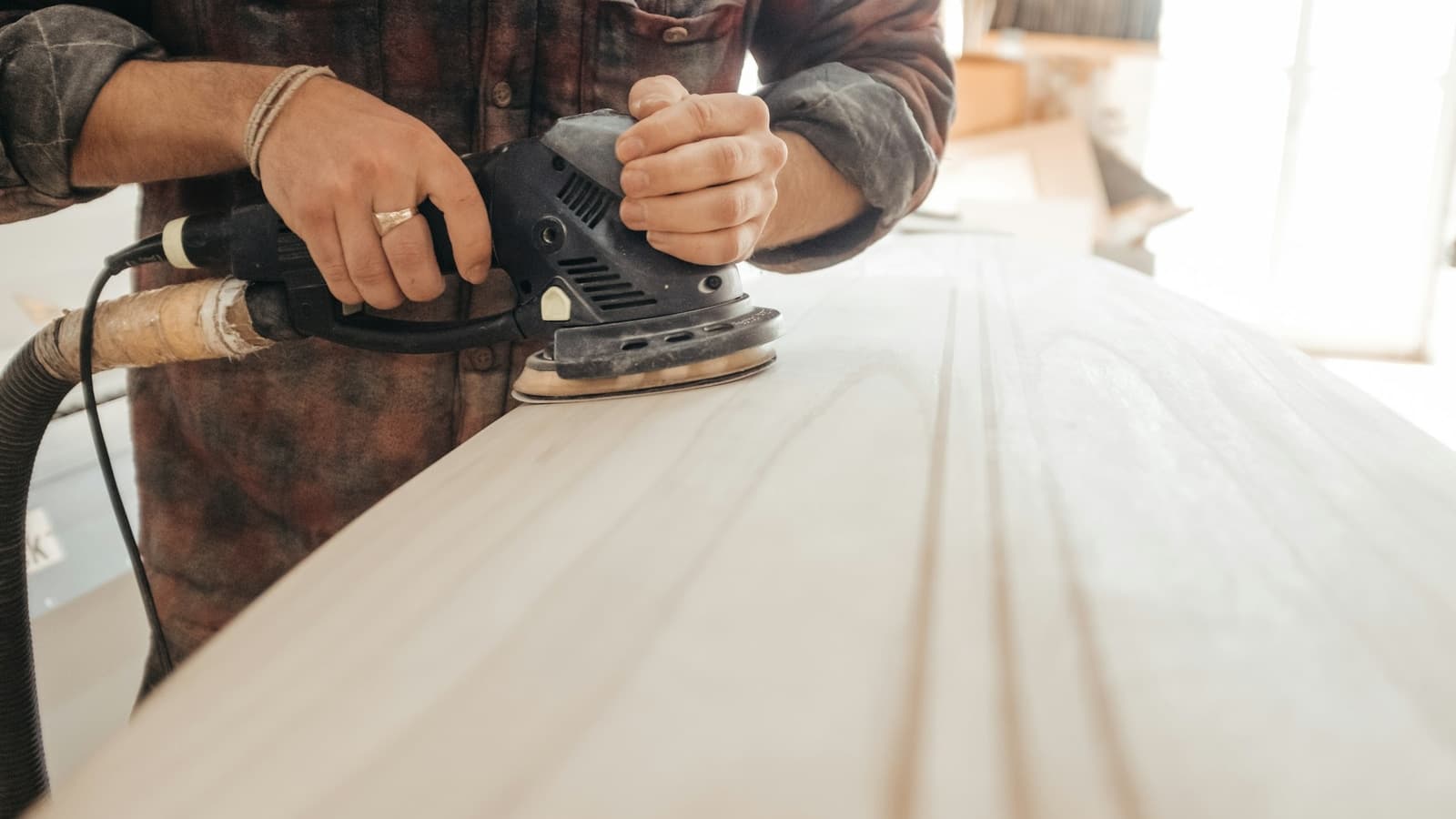 A painter lightly scuff-sanding a cabinet door panel on a workbench before priming