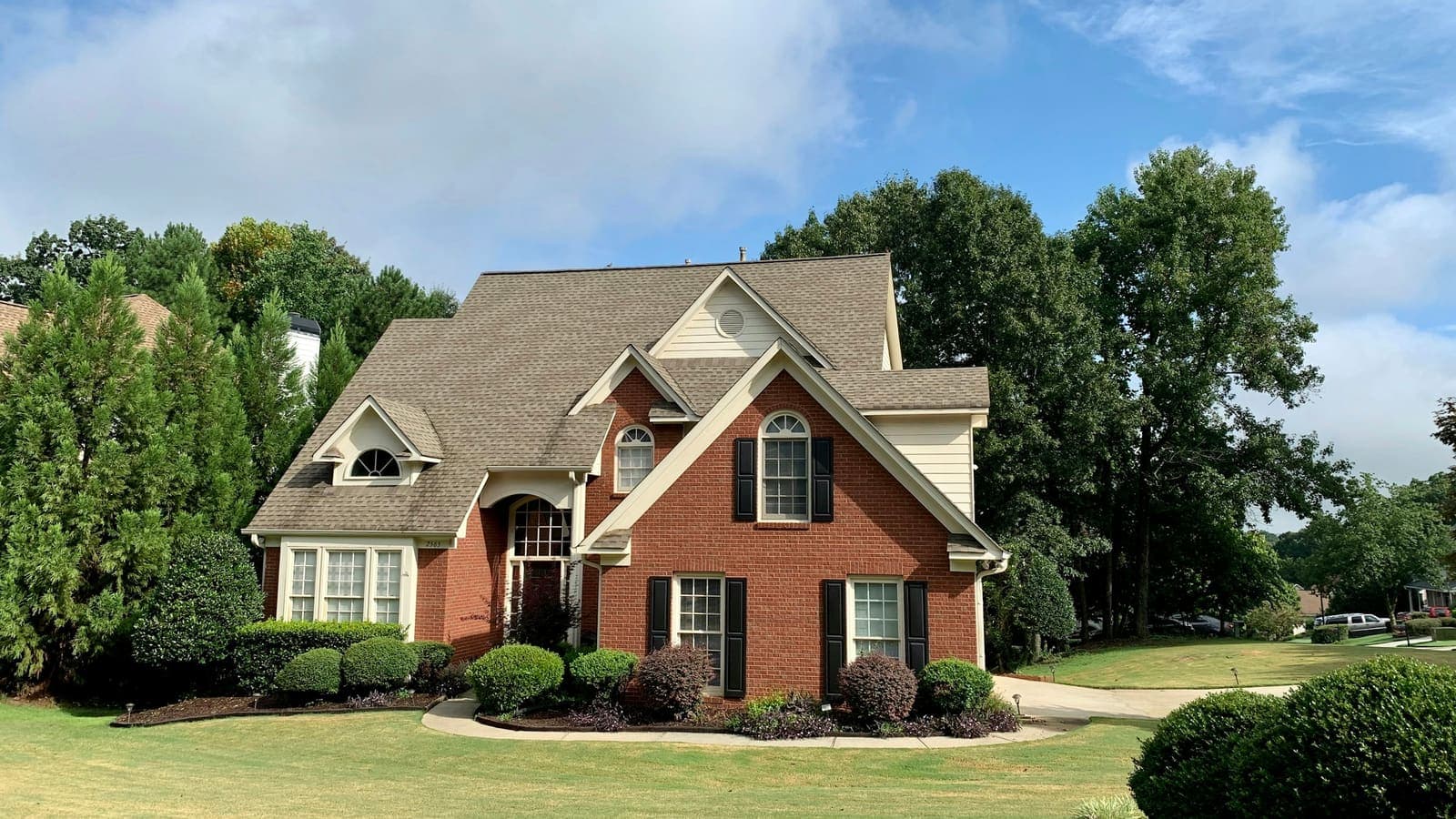 Two-story suburban home with fresh exterior paint, brick body, light trim, and blue sky in afternoon light